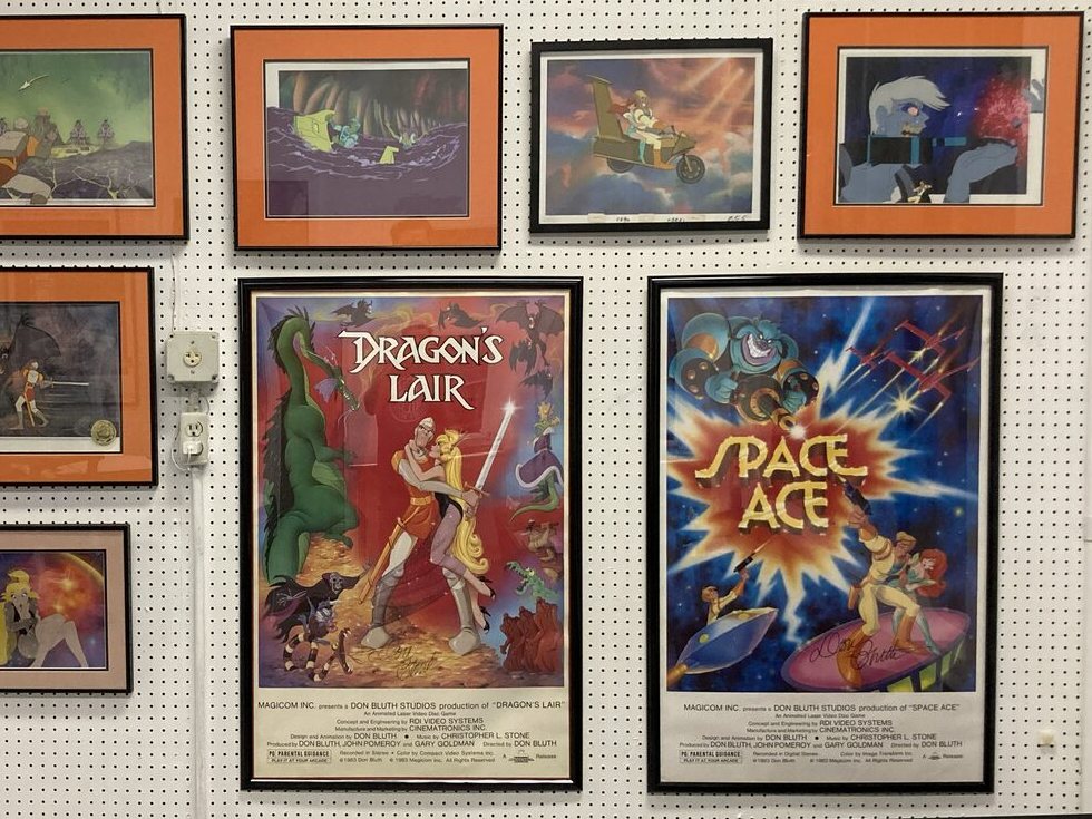 Framed animation cels with Dragon's Lair and Space Ace posters on a pegboard wall