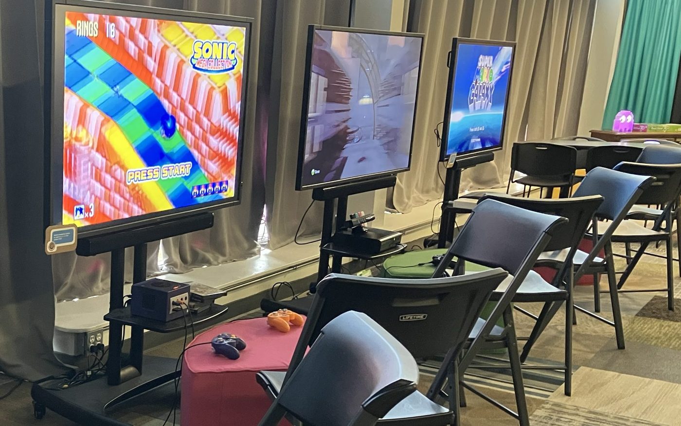 Three flat-screen console setups with GameCube and Xbox consoles, controllers and folding chairs