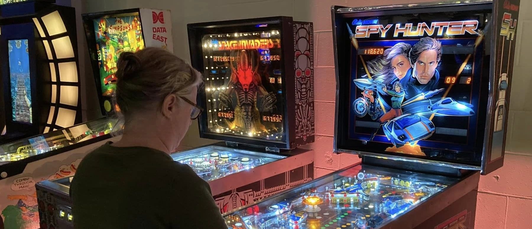 A guest playing Spy Hunter pinball next to Space Invaders and The Simpsons pinball machines